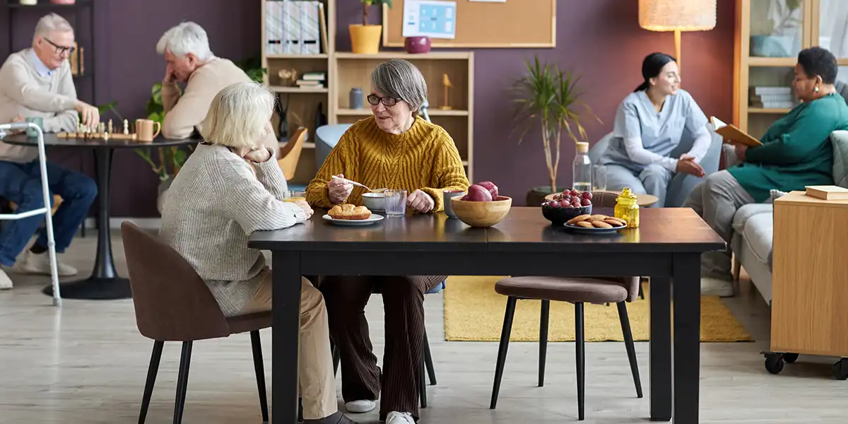 Personas mayores comparten en una sala de actividades, unas conversan y otras juegan...