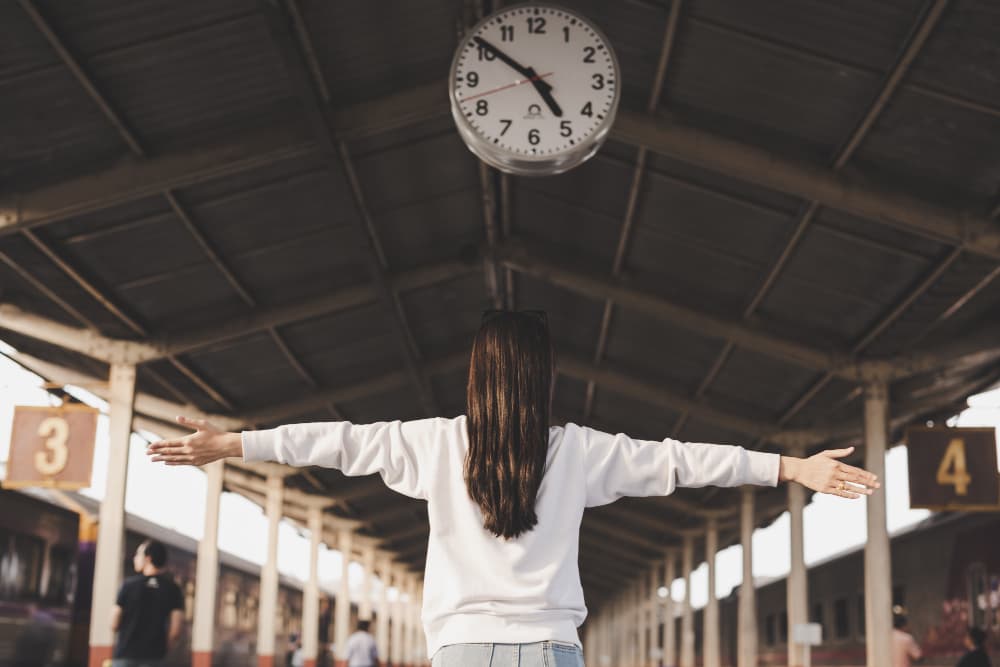 Mujer en estaci&oacute;n de tren frente a un reloj representando los m&uacute;ltiples caminos