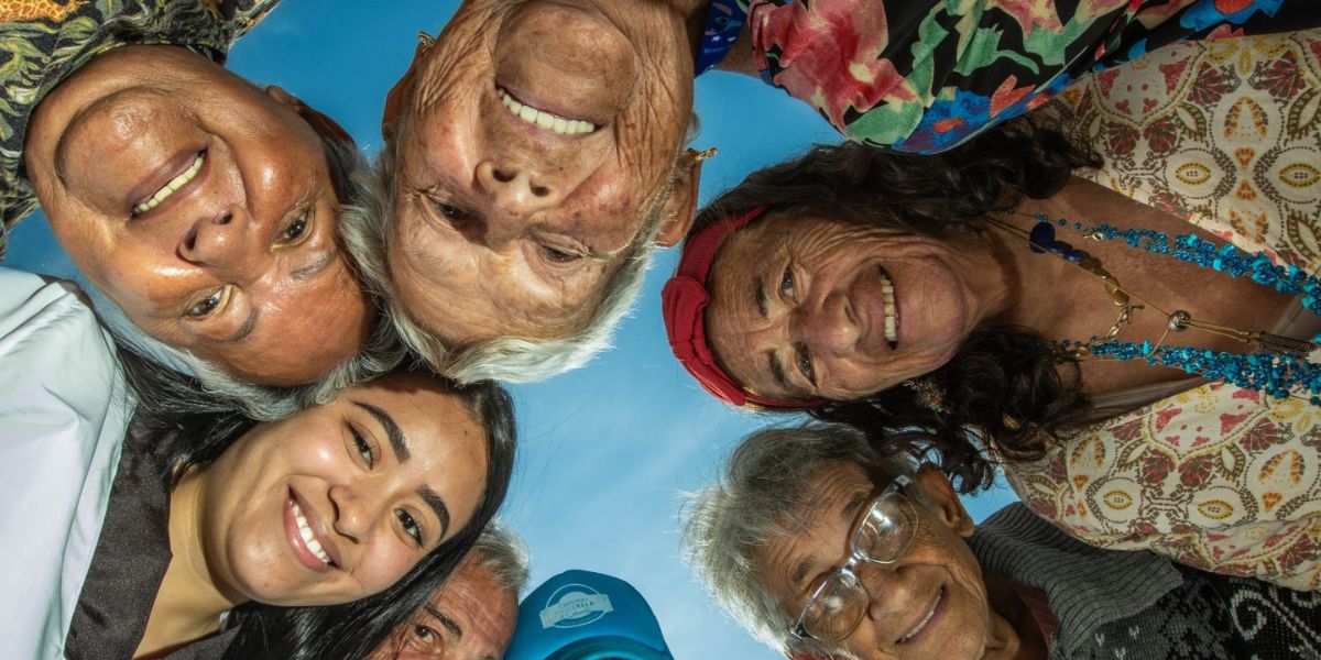Grupo de adultos mayores en c&iacute;rculo, mirando hacia abajo a la c&aacute;mara, con el cielo de fondo.