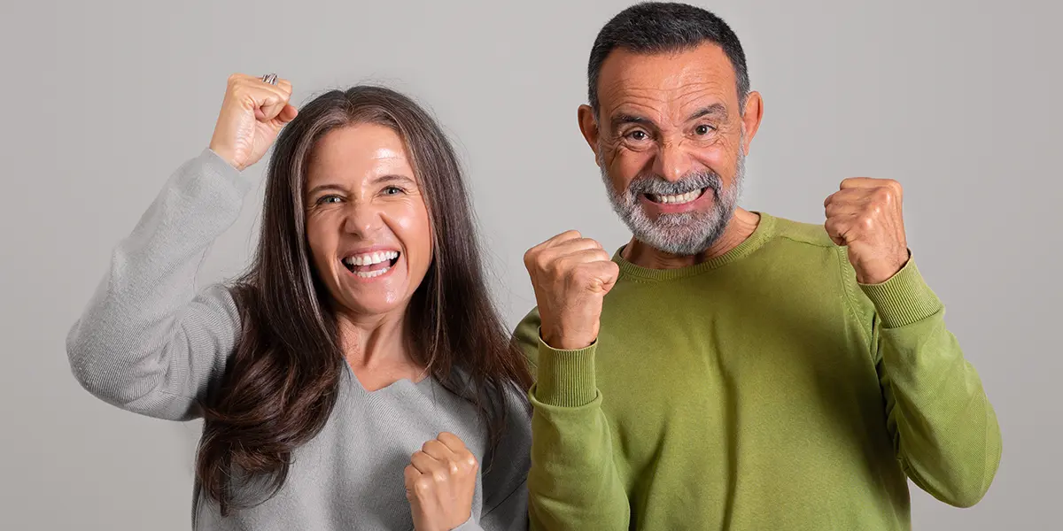 Un hombre y una mujer de aproximadamente 50 a&ntilde;os se r&iacute;en y alzan sus manos en actitud de acci&oacute;n y lucha positiva