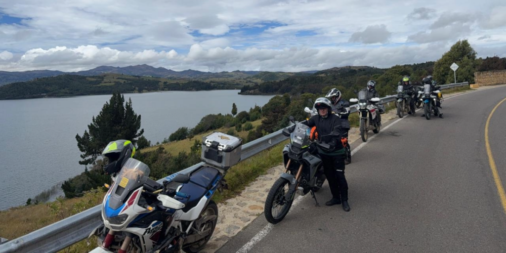 Fotografía de varios moteros veteranos del grupo Moteros Veteranos, estacionados sobre una carretera con un lago de fondo.