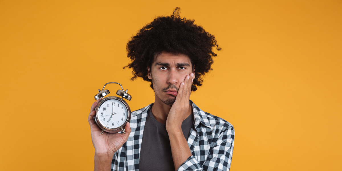 El peso del futuro en un reloj Joven preocupado sostiene un despertador con una mano mientras se toca la mejilla con la otra, gesto de ansiedad.