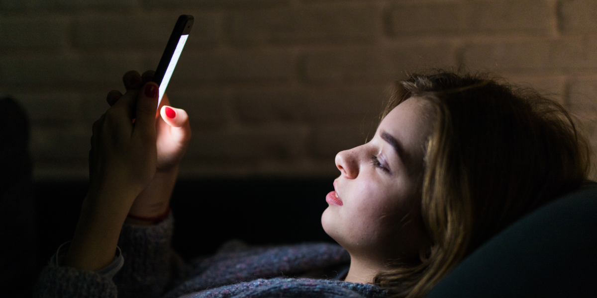 Mujer joven mirando la pantalla de su celular antes de dormir.