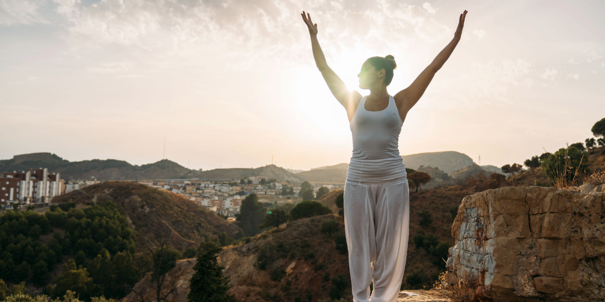 Propósito y movimiento claves para cuidar el cerebro Mujer en yoga con brazos levantados ante una montaña.